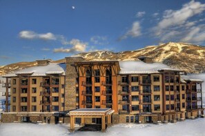Ein mehrstöckiges Hotel mit einer Steinfassade, Balkonen und Blick auf schneebedeckte Berge.