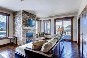 Ein Wohnzimmer mit Kamin aus Stein, einem darüber montierten Fernseher, einer Couch und einem Esstisch.