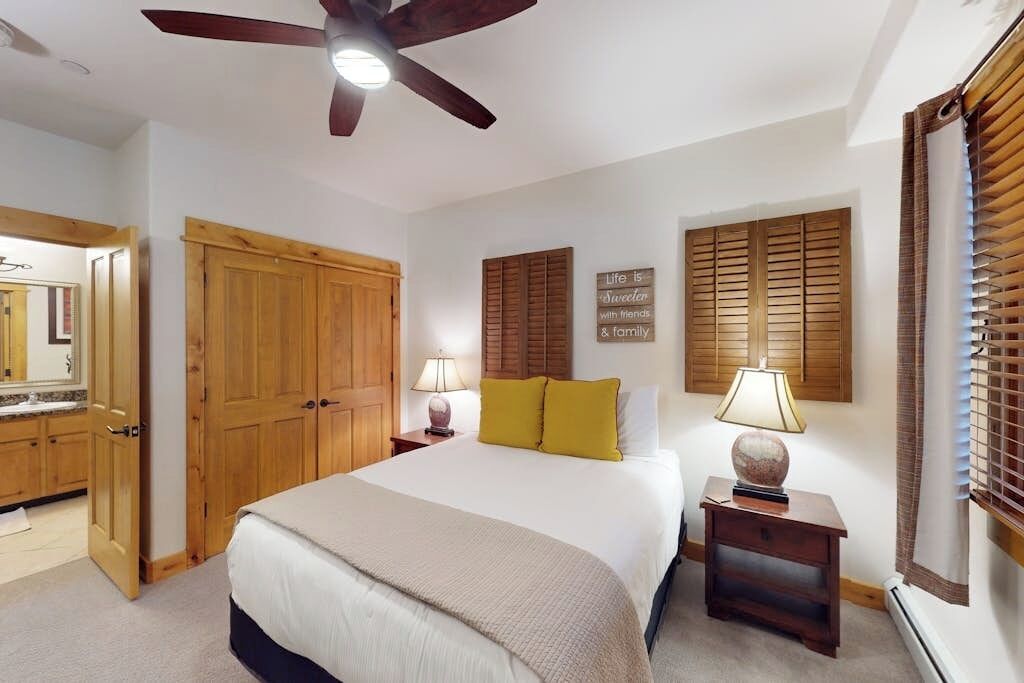 Ein Schlafzimmer mit einem Bett, einem Holzschrank, zwei Nachttischen mit Lampen, einem Deckenventilator und einer Wand mit einem dekorativen Schild.