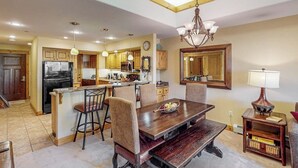 A kitchen with wooden cabinets, a dining table, and chairs. - Canyon Creek A304 - Top-floor mountain condo w/ a shared, heated pool, hot tub, & fitness room (Steamboat Springs)