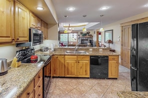 A kitchen with wooden cabinets, granite countertops, a built-in dishwasher, and a black refrigerator. - Top-floor mountain condo w/ a shared, heated pool, hot tub, & fitness room (Steamboat Springs)