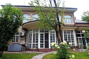 Ein zweistöckiges Haus mit einem bogenförmigen Wintergarten, einer Ziegel-Fassade und einem gepflegten Garten mit weißen Blüten.