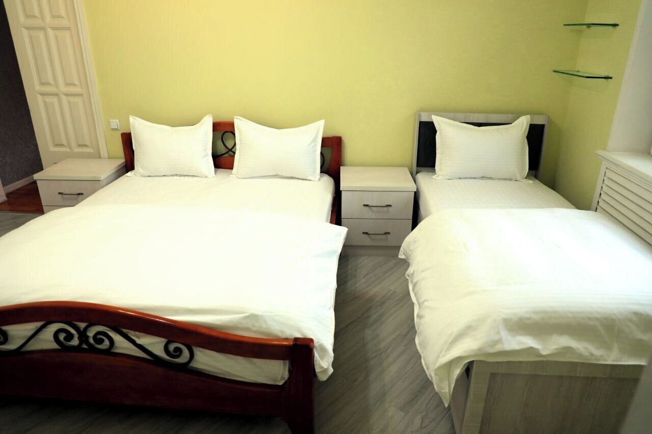 Une chambre d’hôtel avec deux lits simples, des têtes de lit en bois, des tables de chevet avec tiroirs et un plancher de couleur claire.