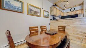 Uma sala de jantar com mesa e cadeiras de madeira, cozinha com armários de madeira e quadros nas paredes.