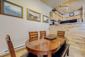 Ein Essbereich mit Holztisch und -stühlen, eine Küche mit Holzausstattung und gerahmte Bilder an der Wand.