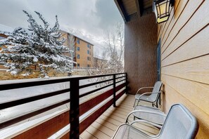 Ein Balkon mit Holzbalkon, Metallstühlen und Blick auf schneebedeckte Gebäude und Bäume.