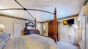 Quarto com cama de dossel, televisão na parede e escrivaninha com abajur.