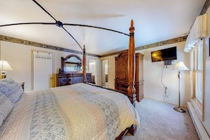 Ein Schlafzimmer mit Himmelbett, einem an der Wand montierten Fernseher und einem Schreibtisch mit Lampe.