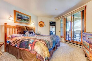 Ein Schlafzimmer mit einem Bett, einer Holzkommode, einem Gemälde und einer Glastür zum Außenbereich.