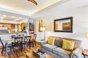 Ein Wohnzimmer mit Sofa, Couchtisch, Esstisch mit Stühlen, Küchenzeile und einem gerahmten Bild an der Wand.