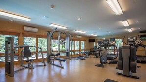 Un gimnasio con equipo de ejercicio diverso, ventanas amplias y un interior de madera.