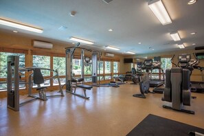 Ein Fitnessstudio mit diversen Trainingsgeräten, großen Fenstern und Holzvertäfelung.