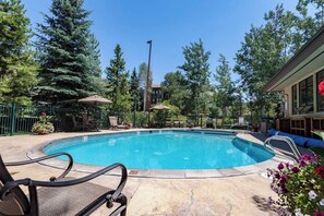 Ein Pool mit Liegestühlen und Sonnenschirmen, umgeben von Bäumen und einem Gebäude.