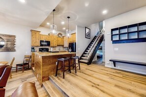 Eine moderne Küche mit Holzschränken, einer zentralen Kochinsel mit Barhocker, einer Treppe und einer eingebauten Bank.