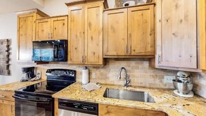 Cucina con mobili in legno, piano di lavoro in granito, lavello in acciaio inox, lavastoviglie, fornello e microonde.