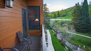 Un edificio in legno con un portico, sedie, una porta che offre una vista e un paesaggio con alberi e un sentiero.