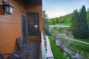 Ein hölzernes Gebäude mit einer Veranda, Stühlen, einer Tür mit Ausblick und einer Landschaft mit Bäumen und einem Weg.