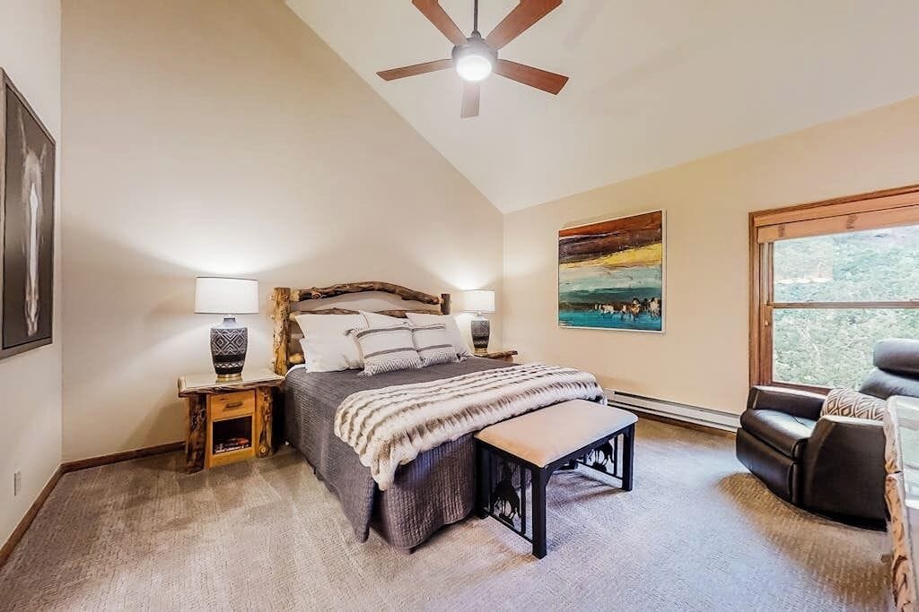 A bedroom with a bed, bedside tables, a bench, a ceiling fan, and a window.