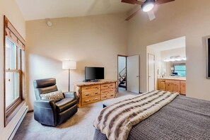 Ein Schlafzimmer mit einem Bett, einem Ledersessel, einer Holzkommode, einem Fernseher und einer Treppe, die in einen weiteren Raum führt.