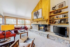 Ein gemütliches Wohnzimmer mit Kamin, roten Sofas, einem Flachbildfernseher und Holzregalen.