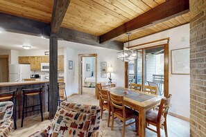 Ein Essbereich mit Holztisch und Stühlen, eine Bar mit Hockern und eine Küche im Hintergrund.
