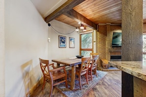 A wooden dining table with chairs, a rug, a brick wall, and a television. - Clean Steamboat suite with washer/dryer, pool & hot tubs - near ski base (Steamboat Springs)