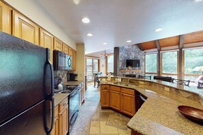 A spacious kitchen with granite countertops, wooden cabinets, a large island, and a stone fireplace. - Spacious Steamboat condo with pool, hot tubs, W/D - close to skiing & hiking (Steamboat Springs)