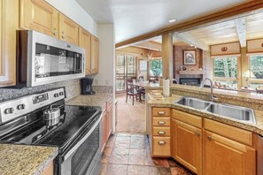 Eine Küche mit Granit-Arbeitsplatten, Holzschränken, einer Edelstahl-Spüle und einer eingebauten Mikrowelle.