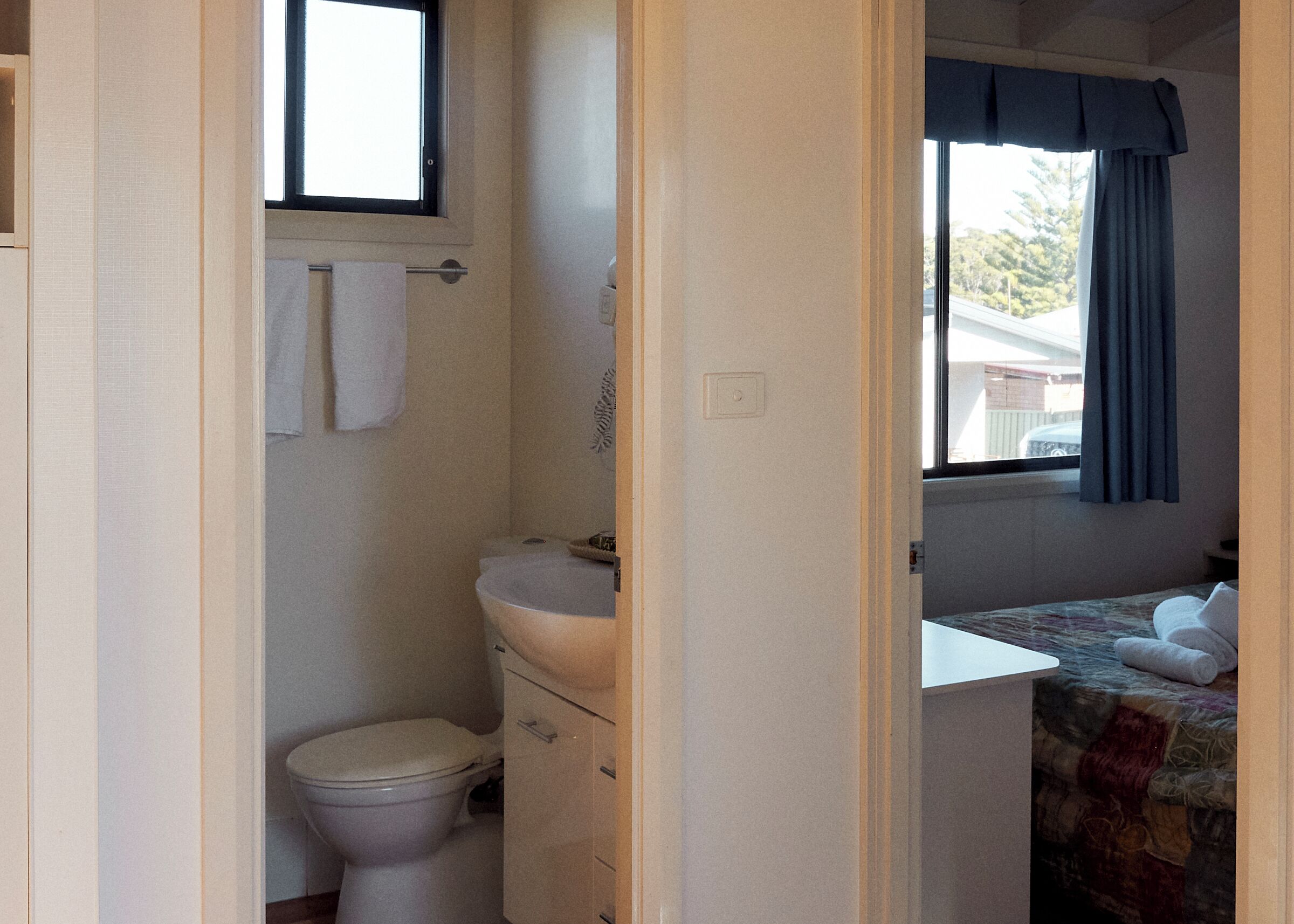 A compact bathroom with a toilet, sink, and a window with curtains.
