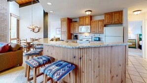 Una cocina con armarios de madera, una isla central y un comedor con sillas.