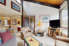 A living room with a television, striped armchairs, a sofa, a coffee table with a dinosaur design, and a bookshelf.