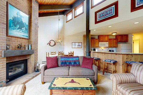 A living room with a fireplace, sofa, coffee table, and kitchen area with wooden cabinets and a bar.