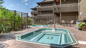 Una piscina con borde de azulejos, una cerca de madera y un edificio con balcones al fondo.