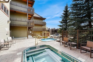 Ein Poolbereich mit Whirlpool, Liegestühlen und einer Treppe, die zu einem Gebäude mit einem Balkon führt.