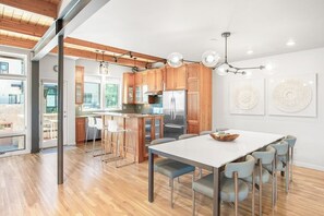 Eine moderne Küche mit Holzschränken, einem Edelstahlkühlschrank und einem Essbereich mit weißem Tisch und Stühlen.