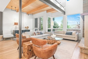 Ein modernes Wohnzimmer mit Holzbalkendecke, großen Fenstern und einem Kamin aus Stein.
