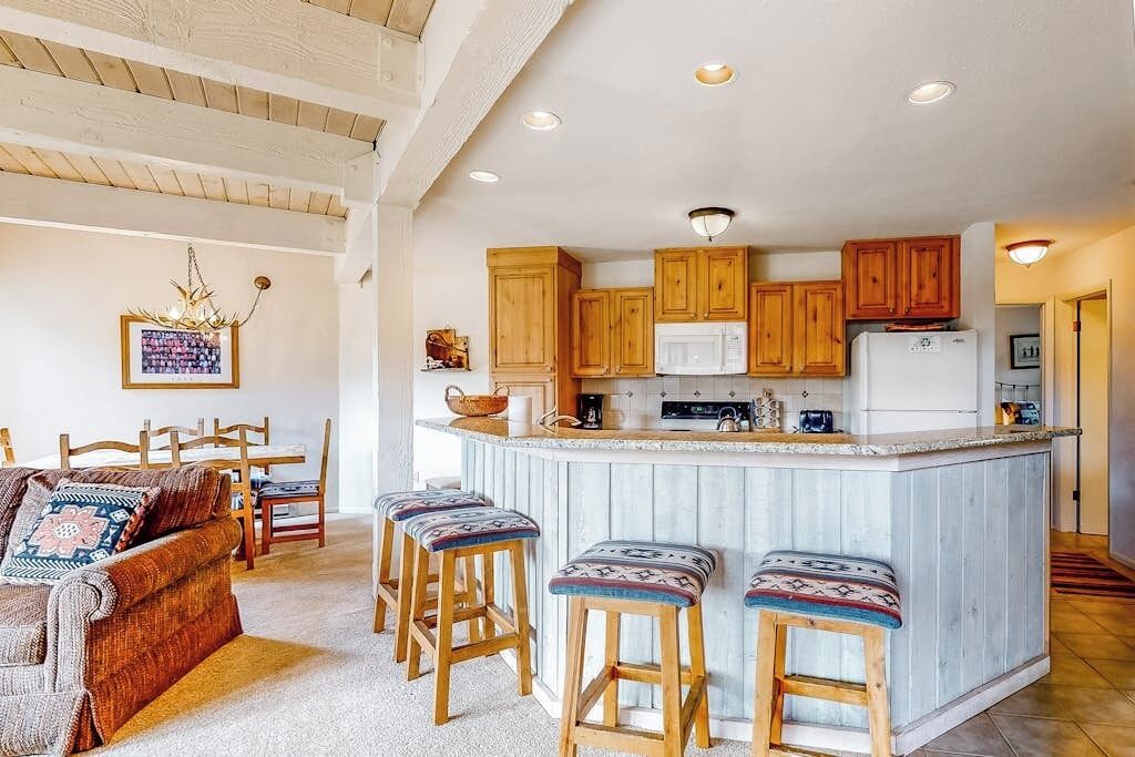 Una cocina con armarios de madera, un refrigerador blanco y una zona de bar con taburetes.