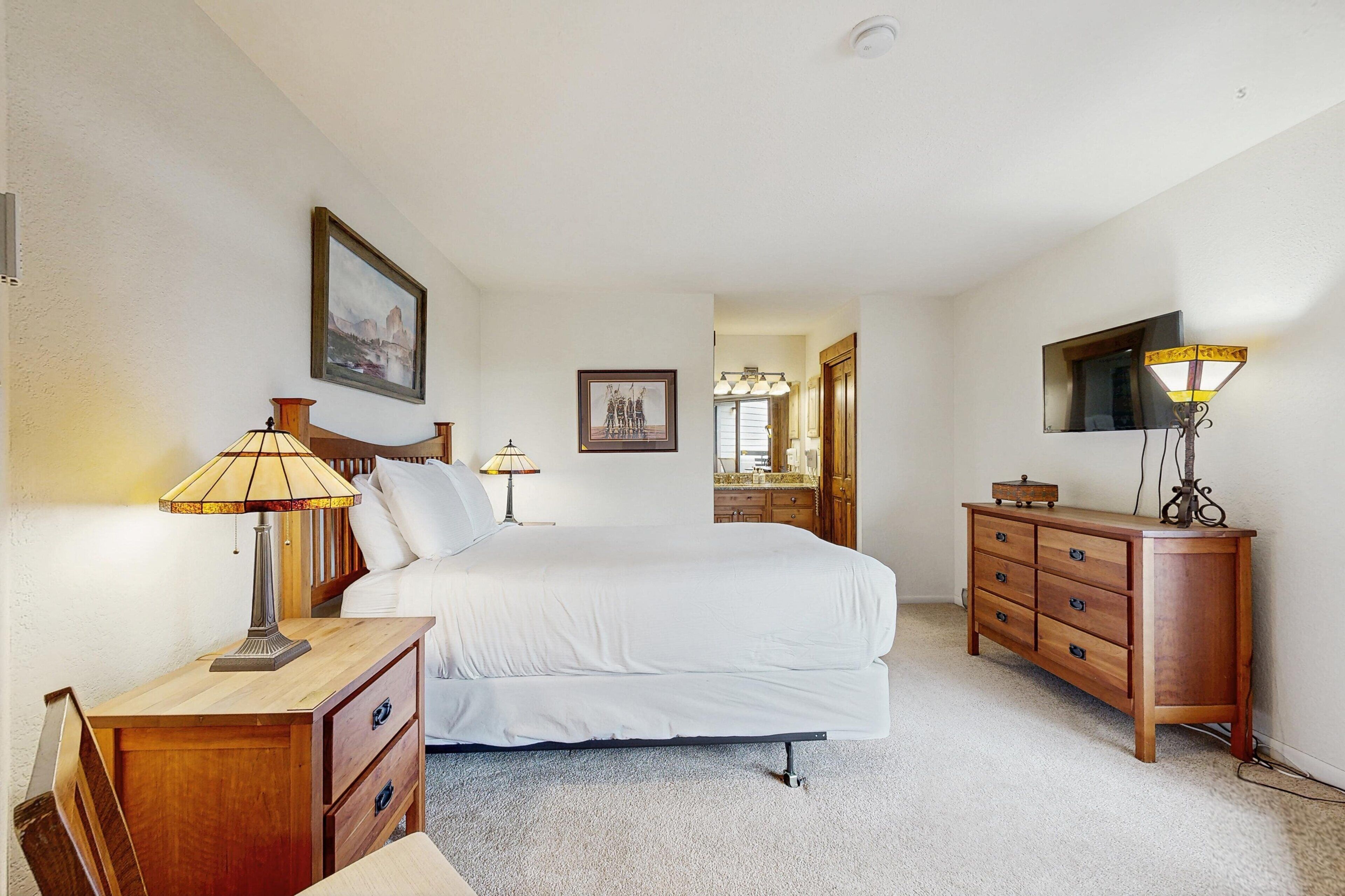 A bedroom with a bed, bedside tables, a dresser, a TV, and a framed picture on the wall.