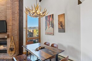 Ein Essbereich mit Holztisch, Stühlen, Kamin, einer Chandelier und Blick ins Freie.