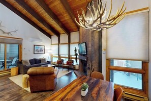 Ein geräumiges Wohnzimmer mit Kamin, einem großen Esstisch aus Holz und einem Fernseher.