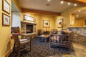 Ein gemütlicher Lounge-Bereich mit Kamin aus Stein, Holzmöbeln und gerahmten Bildern an den Wänden.