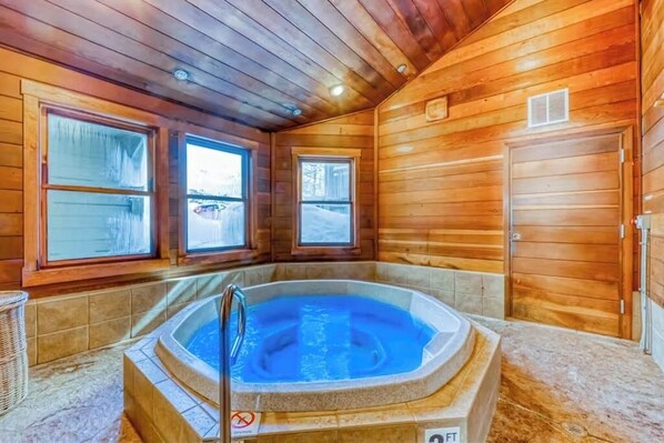Ein Holzblockhaus-Innenraum mit Whirlpool, großen Fenstern und einer Tür.