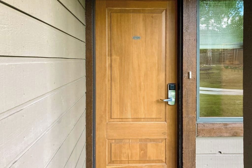 A wooden door with a metal handle and a keyhole, a number plate, and a window with a view of a lawn.