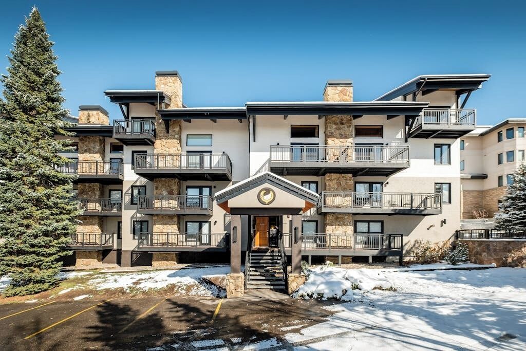 A multi-story hotel with balconies, a central entrance, and a snowy ground.