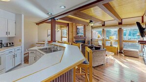 Una cocina moderna con una isla central, un comedor con suelo de madera y ventanas amplias que dejan entrar luz natural.