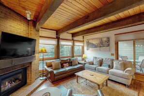 Ein gemütliches Wohnzimmer mit Kamin, Ledersofas, einem Couchtisch und großen Fenstern.