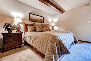 A bedroom with a bed, two bedside tables, a nightstand, a lamp, and a framed picture on the wall. - Luxury Ski-In/Ski-Out Studio w/ Balcony, WiFi, Shared Hot Tub - Walk to Gondola (Steamboat Springs)