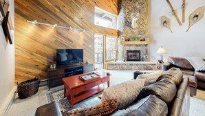 A living room with a stone fireplace, wooden ceiling, and a television. - Top-Floor, Ski-In/Ski-Out Condo w/ Loft, Fireplace, Balcony & Shared Hot Tub (Steamboat Springs)