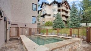 A swimming pool with a stone border, a wooden fence, and a building with balconies in the background. - Top-Floor, Ski-In/Ski-Out Condo w/ Loft, Fireplace, Balcony & Shared Hot Tub (Steamboat Springs)