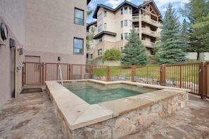 A swimming pool with a stone border, a wooden fence, and a building with balconies in the background. - Top-Floor, Ski-In/Ski-Out Condo w/ Loft, Fireplace, Balcony & Shared Hot Tub (Steamboat Springs)
